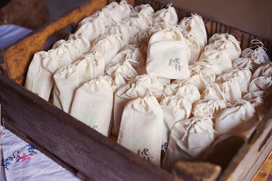 A wooden crate filled with small drawstring bags, branded with initials