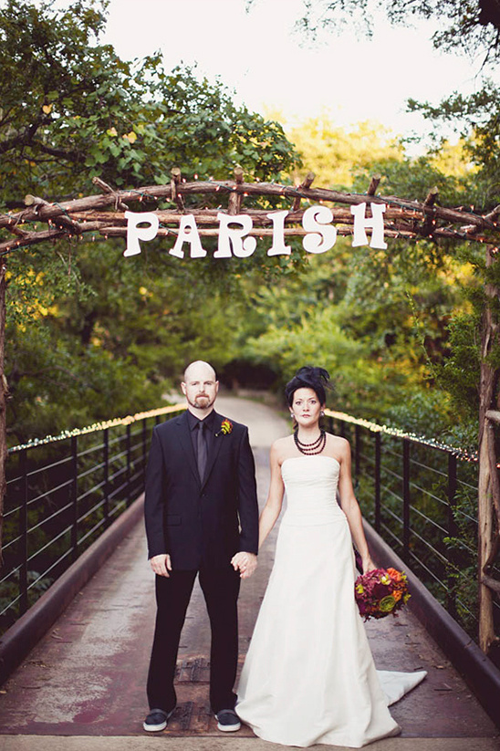 A stylish couple stands on bridge under Parish sign at a wedding