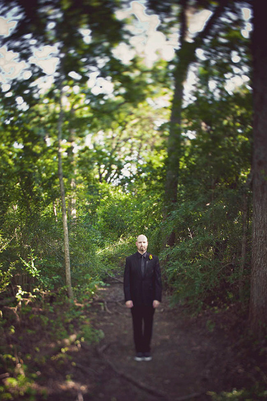 Man in a black suit stands on a trail surrounded by green trees
