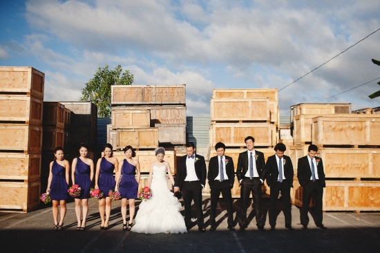 Wedding party posing in front of wooden crates under a cloudy sky