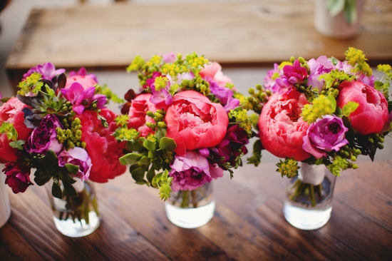 Vibrant pink and purple floral bouquets in glass jars on wooden table