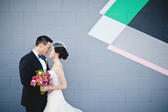Elegant wedding couple embraces near a modern geometric mural