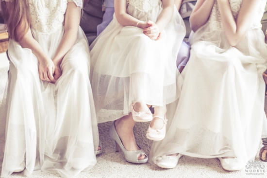 Three girls in white dresses sit, showing their shoes and dresses
