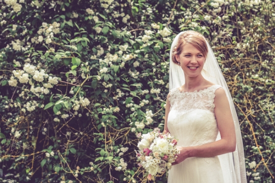 Smiling bride in white dress and veil holding a flower bouquet