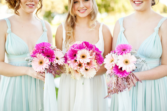 Bridesmaids with bouquets of pink gerbera daisies smile at the camera