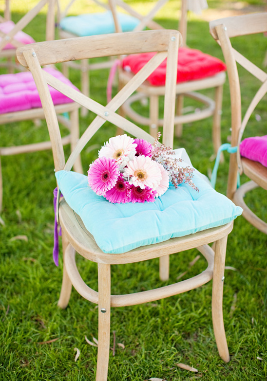A wooden chair adorned with flowers and vibrant cushions on green grass