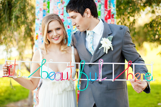 Smiling couple holding a colorful it is beautiful here sign