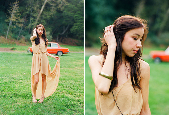 Woman in a flowing dress posing with an orange vintage car on the grass