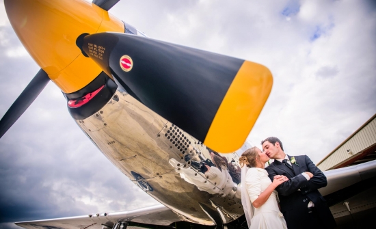 Wedding couple kissing by a vintage airplane with a yellow propeller