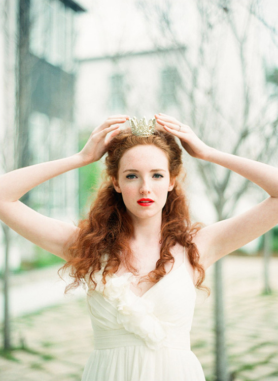 Beautiful redhead woman placing a golden crown on her head