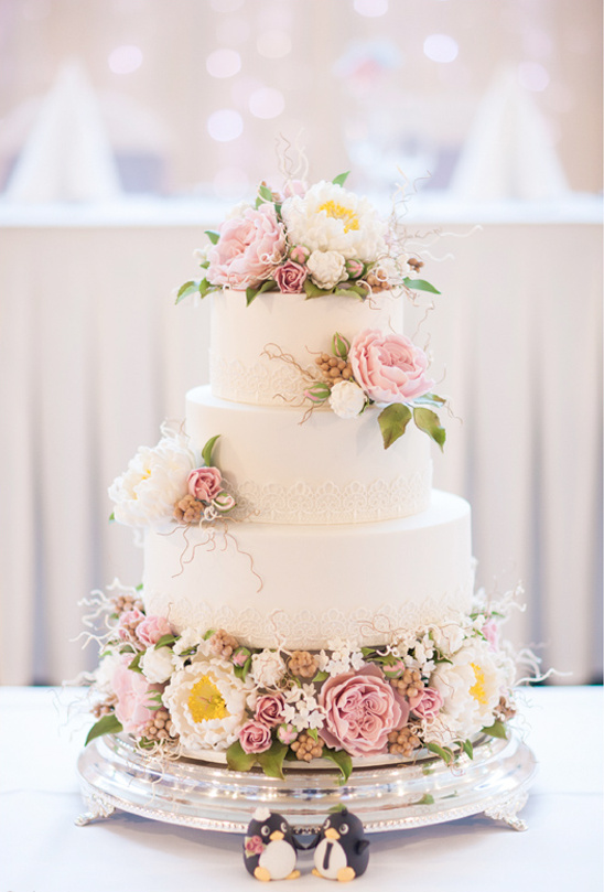 Three tier wedding cake adorned with flowers and penguins