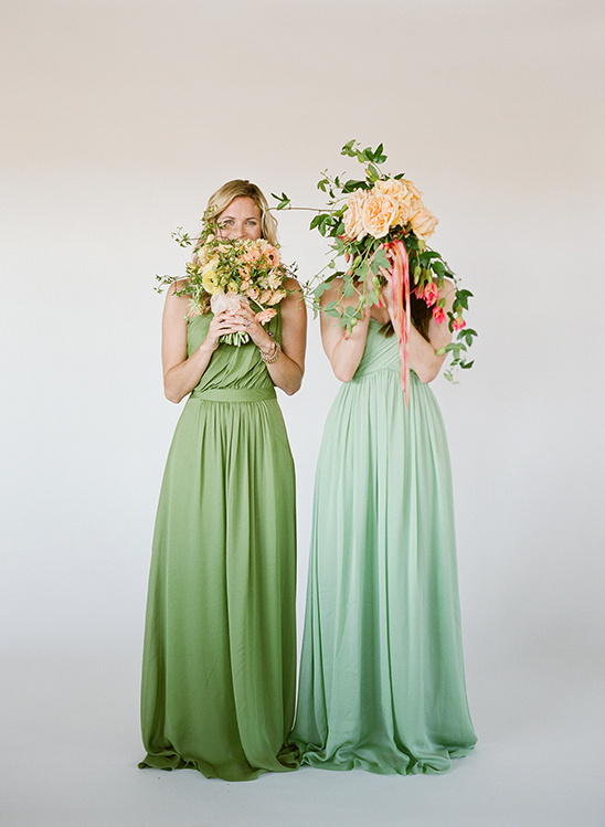 Two women in green bridesmaid dresses holding floral bouquets