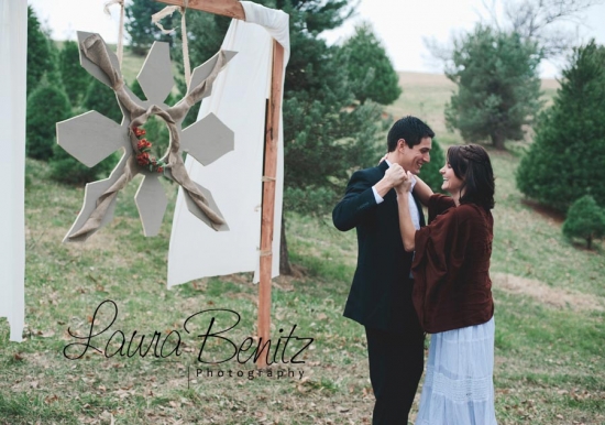 Couple embracing near rustic snowflake decor at Christmas tree farm