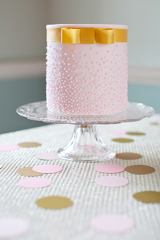 Pink cake with gold ribbon on decorative cake stand