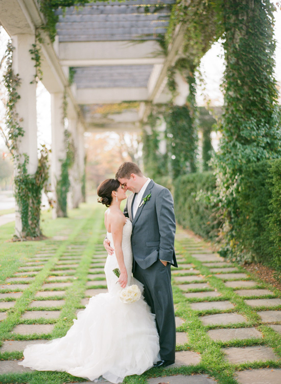 Bride and groom embrace under a vine-covered pergola