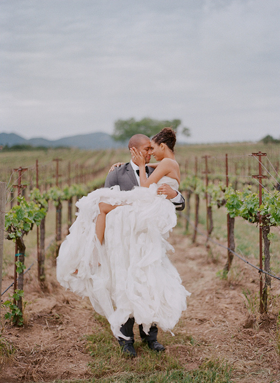 Groom happily carries bride in vineyard
