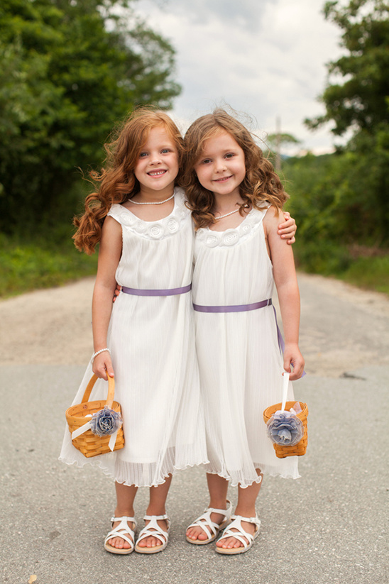 Two flower girls in white dresses embrace smiling