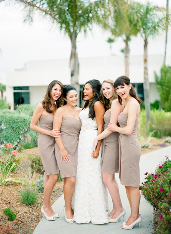 Bride and bridesmaids in taupe dresses smiling outdoors