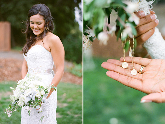 Bride in lace dress holds bouquet and initial necklaces