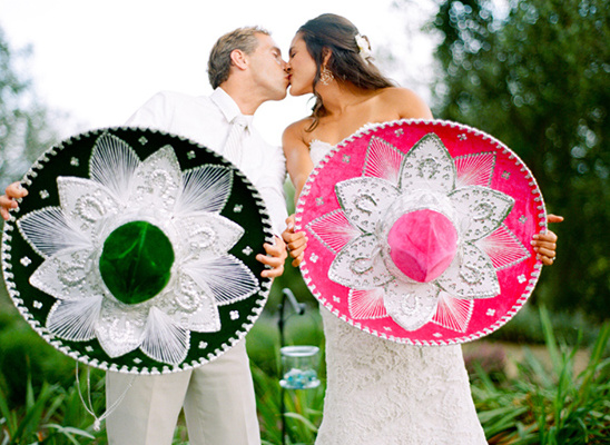 Kissing bride and groom holding vibrant sombreros