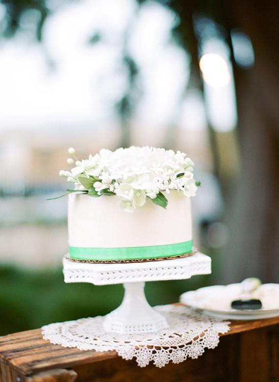Elegant white wedding cake adorned with white flowers and a mint ribbon
