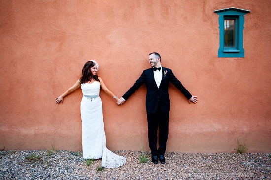 Bride and groom holding hands against orange wall