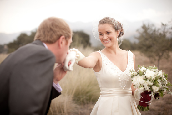 Bride smiling as groom kisses her gloved hand