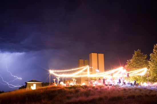 Nighttime event illuminated by string lights under a stormy sky