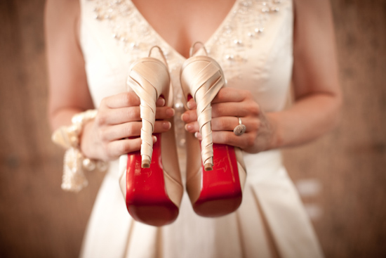 Bride holds red bottom wedding shoes in dress