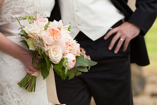 Bride holds peach rose bouquet near groom at wedding
