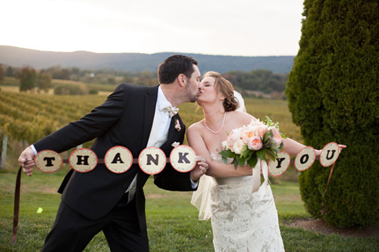 Newlyweds share a kiss, holding a Thank You banner