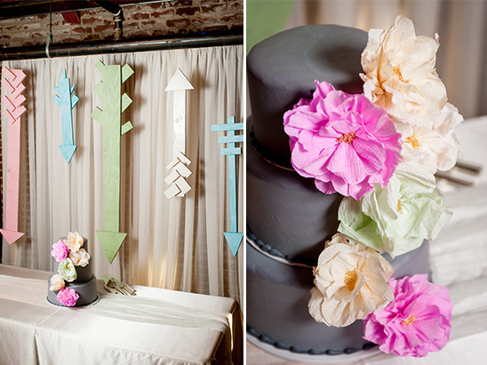 Stylish wedding cake with flowers and arrow decorations on the wall