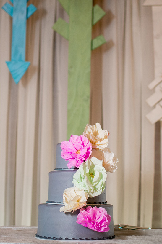 Three-tiered gray cake with vibrant floral decorations, a delicious treat