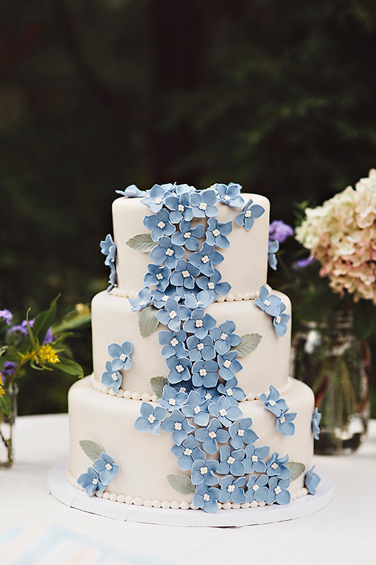 Three tier wedding cake adorned with blue hydrangea flowers