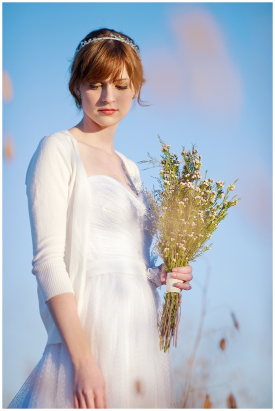 Elegant bride in white dress holding a flower bouquet under a blue sky