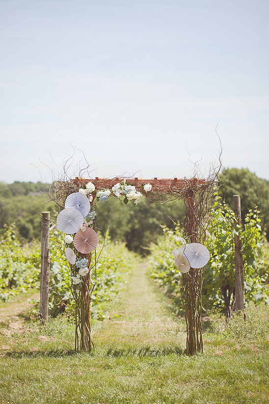 Wedding arch decorated with fans and flowers at vineyard aisle