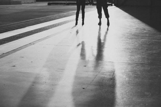Two people walk with long shadows on a sunlit concrete