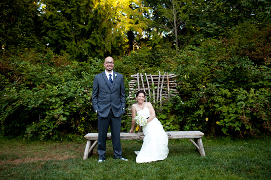 Wedding couple poses for photo on a bench in a green garden