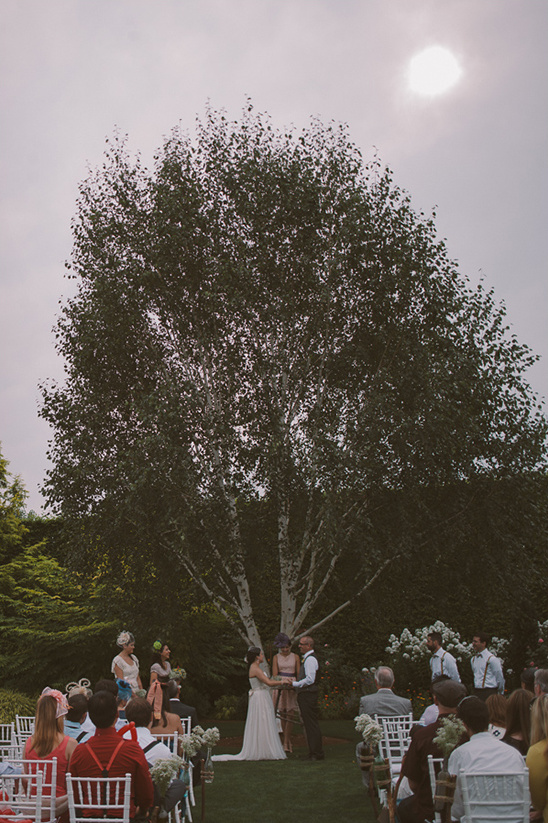 Wedding ceremony under a big tree with guests gathered outside
