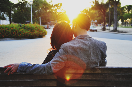 Couple enjoying sunset on a park bench, romantic embrace