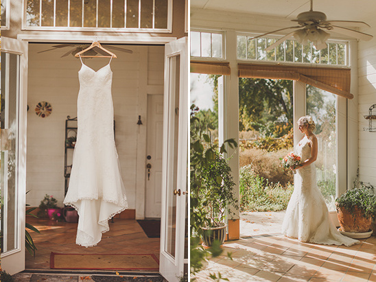 Wedding dress hanging and bride with bouquet standing in sunlight
