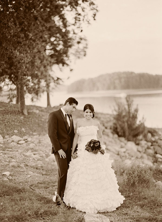 Sepia toned photo of a happy newlywed couple holding hands near lake