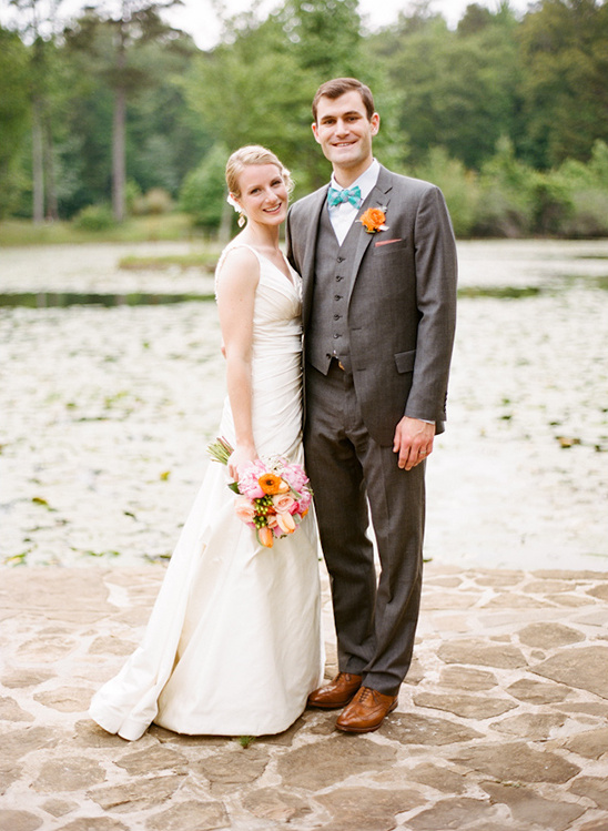 Happy wedding couple standing together by a lake, smiling for the camera
