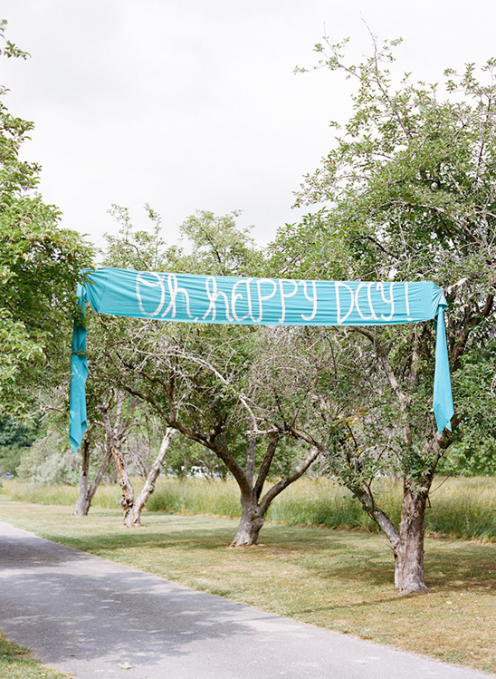 Oh Happy Day banner strung between trees in a park setting