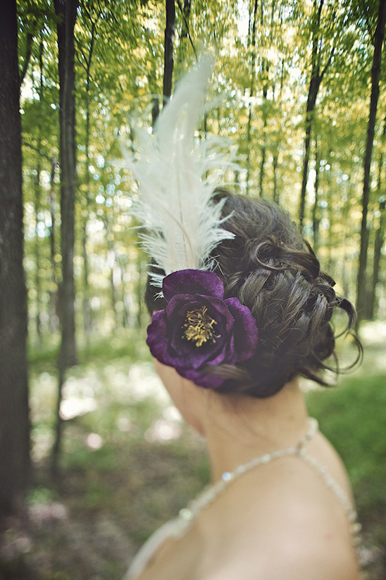 Bride wearing a beautiful purple flower and feather hairpiece in the woods