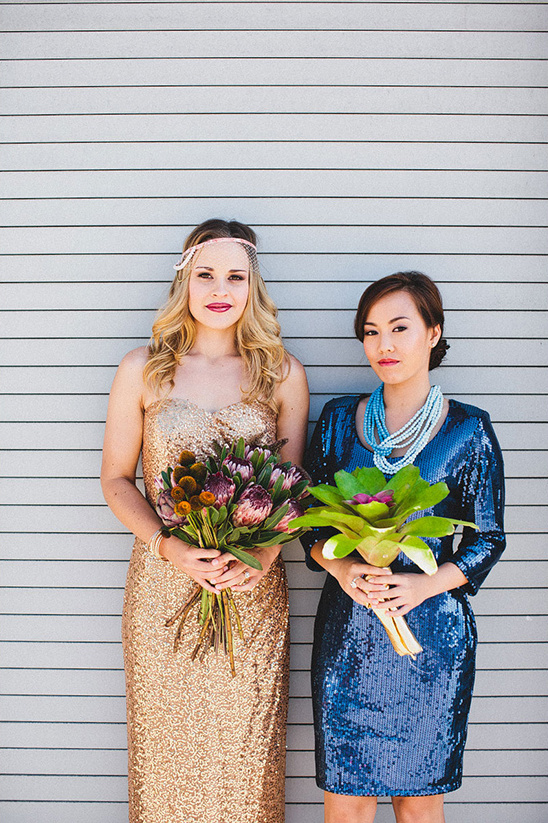 Two women in sequined dresses hold bouquets and smile
