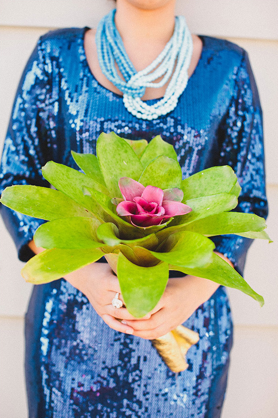 Woman in a blue sequin dress holding a unique green and pink flower