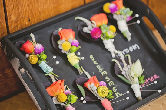 colorful boutonnieres wrapped in yarn and on a chalkboard tray