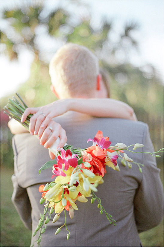 Bride embraces groom holding colorful orchid bouquet