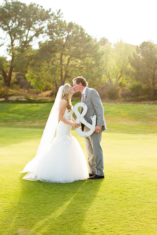 Bride and groom share a kiss holding a wedding anchor on the green grass